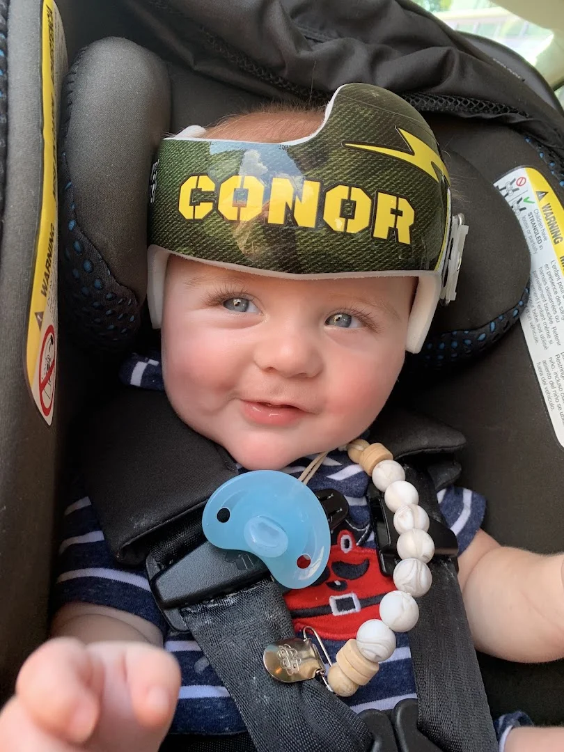 Baby wearing a custom-wrapped DOC band helmet with name and camo design